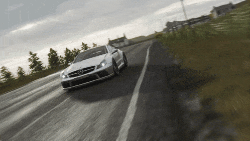a white mercedes is driving down a road with trees in the background