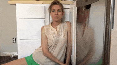 a woman is sitting in front of a refrigerator with her legs crossed