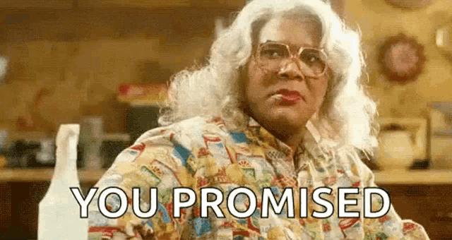 a woman in a wig and glasses is sitting at a table with the words `` you promised '' written on her face .