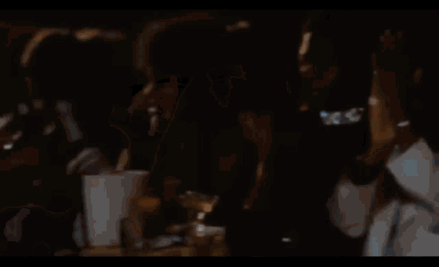 a woman in a black dress is sitting next to a man in a pink jacket in a dark room .