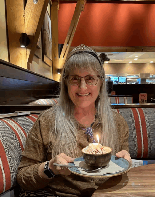 a woman sitting at a table holding a bowl of food with a lit candle
