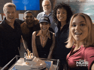 a group of people posing in front of a cake that says ncis on it