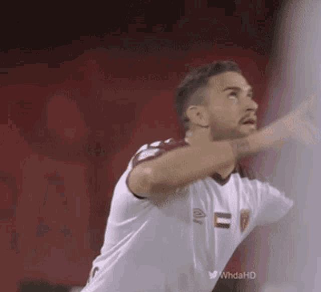 a man in a white shirt is playing soccer on a red field and looking up .