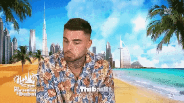 a man in a floral shirt is sitting on a beach in front of a dubai city