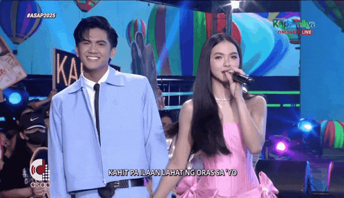 a man in a blue jacket and a woman in a pink dress are on stage holding hands