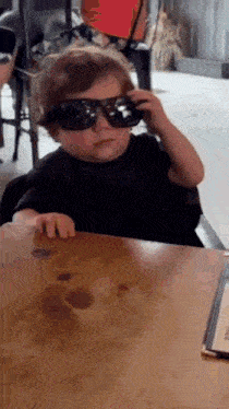 a young boy wearing sunglasses sitting at a table