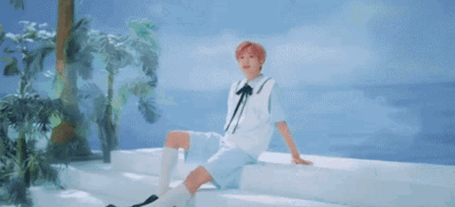 a young man is sitting on a white ledge next to the ocean .