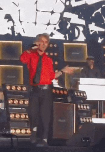 a man in a red shirt and tie stands on a stage