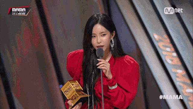 a woman in a red dress is holding a trophy and speaking into a microphone at a mama event