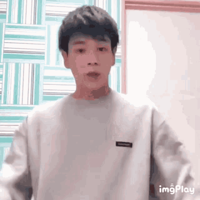 a young man in a white sweater is standing in front of a wall with a striped pattern .