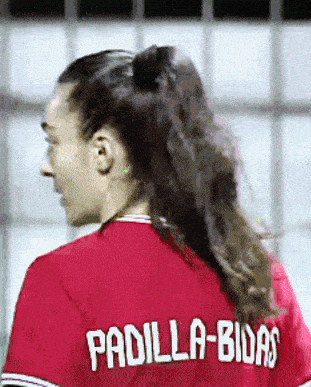 a woman wearing a red padilla-bidas jersey looks over her shoulder