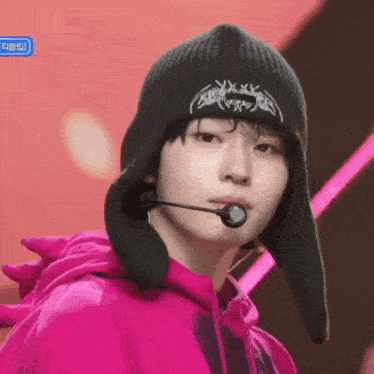 a young man wearing a pink hoodie and a black beanie with a microphone in his mouth .
