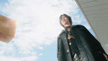 a man in a black coat stands in front of a cloudy sky