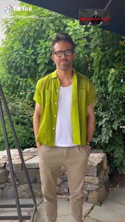 a man wearing a green shirt and khaki pants is standing in front of a bush with a tiktok logo above his head