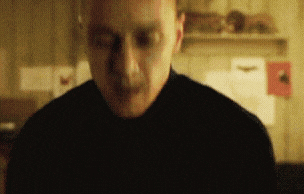 a man in a black shirt is standing in a dark room with his eyes closed .