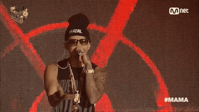 a man wearing a beanie and sunglasses sings into a microphone with the hashtag #mama on the bottom