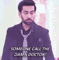 a man with a beard and tie is standing in front of a wall and says `` someone call the damn doctor ! ''