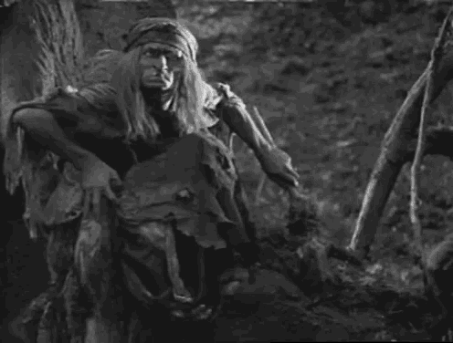 a black and white photo of a man standing next to a tree trunk .