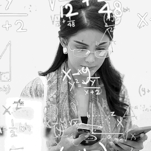 a woman wearing glasses is looking at a cell phone with math equations written on the wall behind her