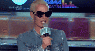 a woman wearing sunglasses is speaking into a microphone in front of a sign that says rama theatre