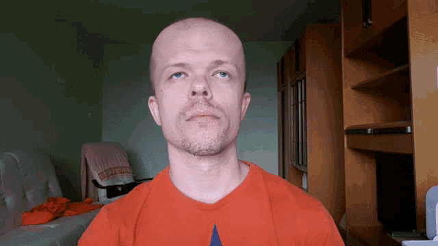 a bald man with a beard wears an orange shirt with the word united on it