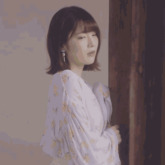 a woman in a floral dress is standing in front of a wooden door
