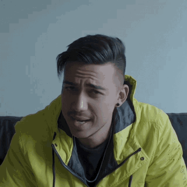 a young man wearing a yellow jacket with a hood looks at the camera