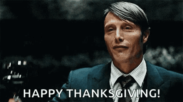 a man in a suit and tie is holding a glass of wine and says happy thanksgiving .