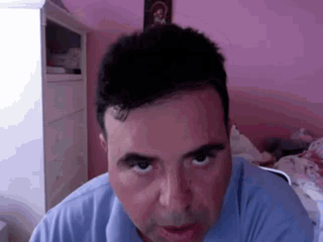 a man in a blue shirt is looking at the camera in a pink room .