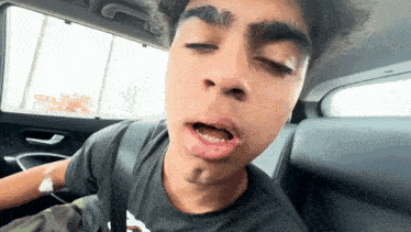 a young man sitting in a car with his eyes closed and his mouth open