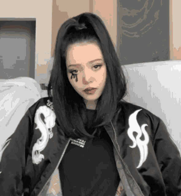 a woman is sitting on a couch wearing a black jacket with dragons on it .