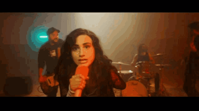 a woman singing into a microphone with a man playing a guitar behind her
