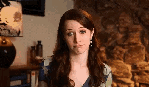 a woman with long red hair is making a funny face in front of a fireplace .