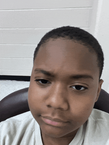 a young boy with a shaved head looks at the camera with a serious look on his face