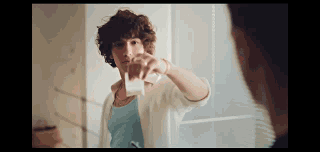 a young man with curly hair is standing in front of a mirror holding a glass of milk .