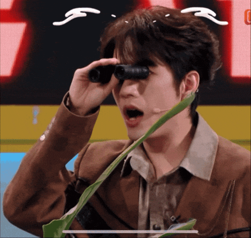 a man in a brown jacket is looking through binoculars with a green plant in his mouth