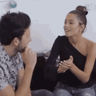 a man and a woman are sitting next to each other on a couch talking to each other .