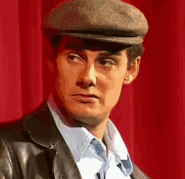 a man wearing a flat cap and a leather jacket is making a funny face .