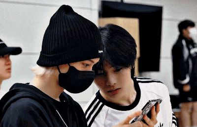 two men wearing masks and beanies are looking at a cell phone