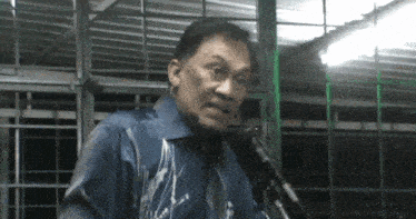 a man in a blue shirt stands in front of a microphone and looks angry