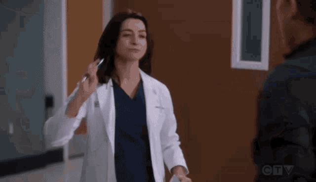 a woman in a lab coat and scrubs is standing next to a man in a hospital hallway .