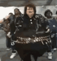 a group of people are dancing in a room with a woman in a leather jacket .