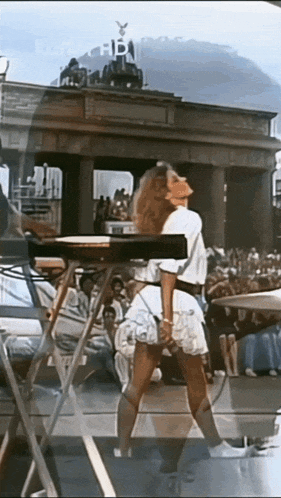 a woman in a white dress is playing a keyboard in front of a crowd of people