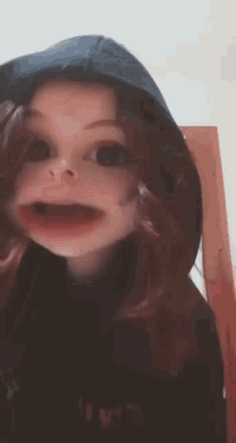 a young girl wearing a hoodie and a hat is making a face .