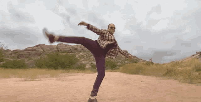a man in a plaid shirt and purple pants is doing a trick in the dirt .