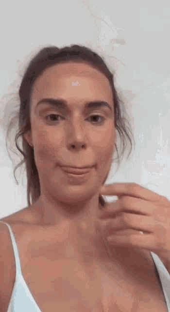 a woman in a white tank top is making a funny face while holding something in her hand .