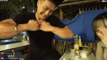 a man and a woman are sitting at a table with bottles on it and a blue tarp in the background ..