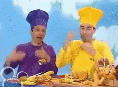 two men wearing chef hats are sitting at a table with food .