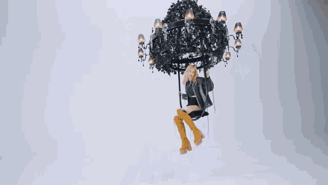 a woman is sitting on a swing under a chandelier hanging from the ceiling