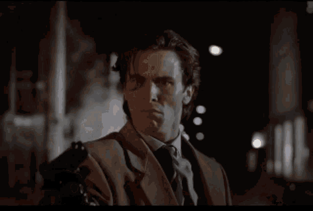 a man in a tan suit and black gloves holds his head